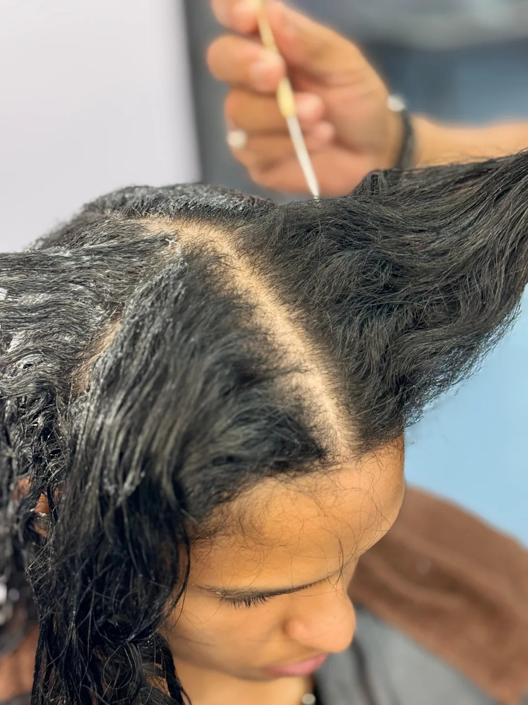 During an anti-frizz smoothing treatment: stylist applying product to a section of hair with a brush at Beyond Salon in Condado
