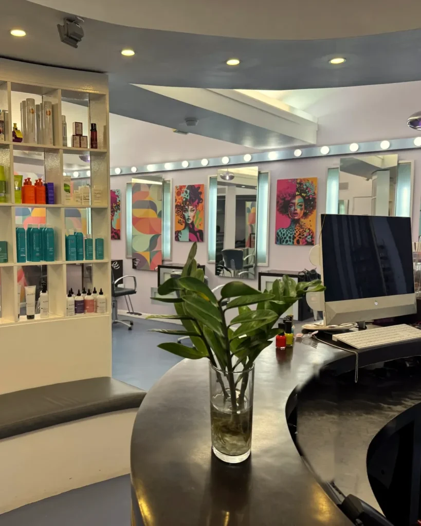 Mostrador de recepción y estantes de productos en Beyond Salon, en Condado, San Juan, con obras de arte coloridas y estaciones de peinado al fondo