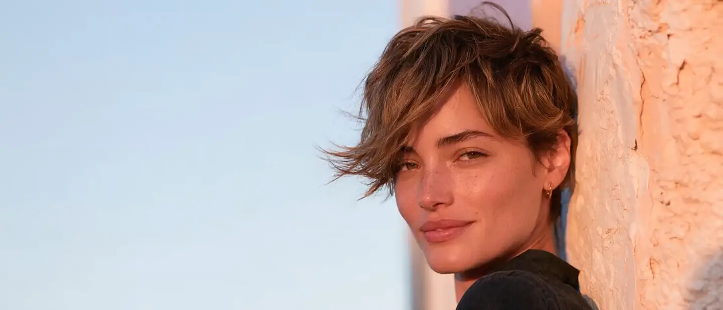 Mujer con un corte pixie texturizado corto bajo la luz de la hora dorada frente a un muro soleado del Viejo San Juan